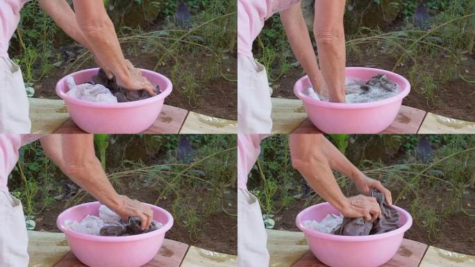 老妇人双手在粉红色的塑料碗中洗衣服