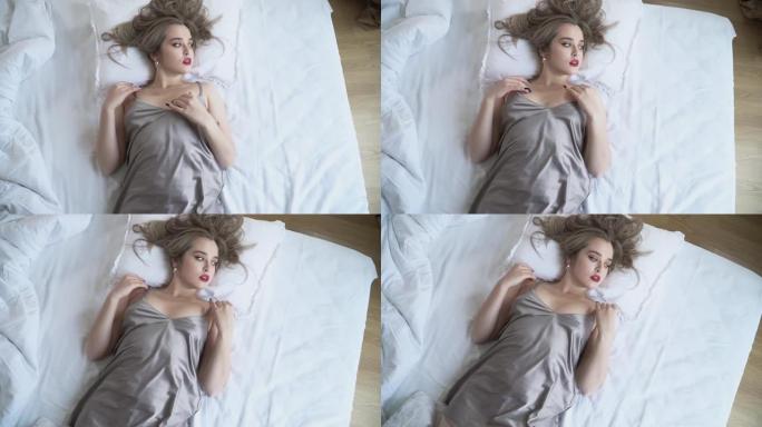 漂亮妆的漂亮女孩躺在床上的背上穿着短睡衣。摄像机从脚移到头部。