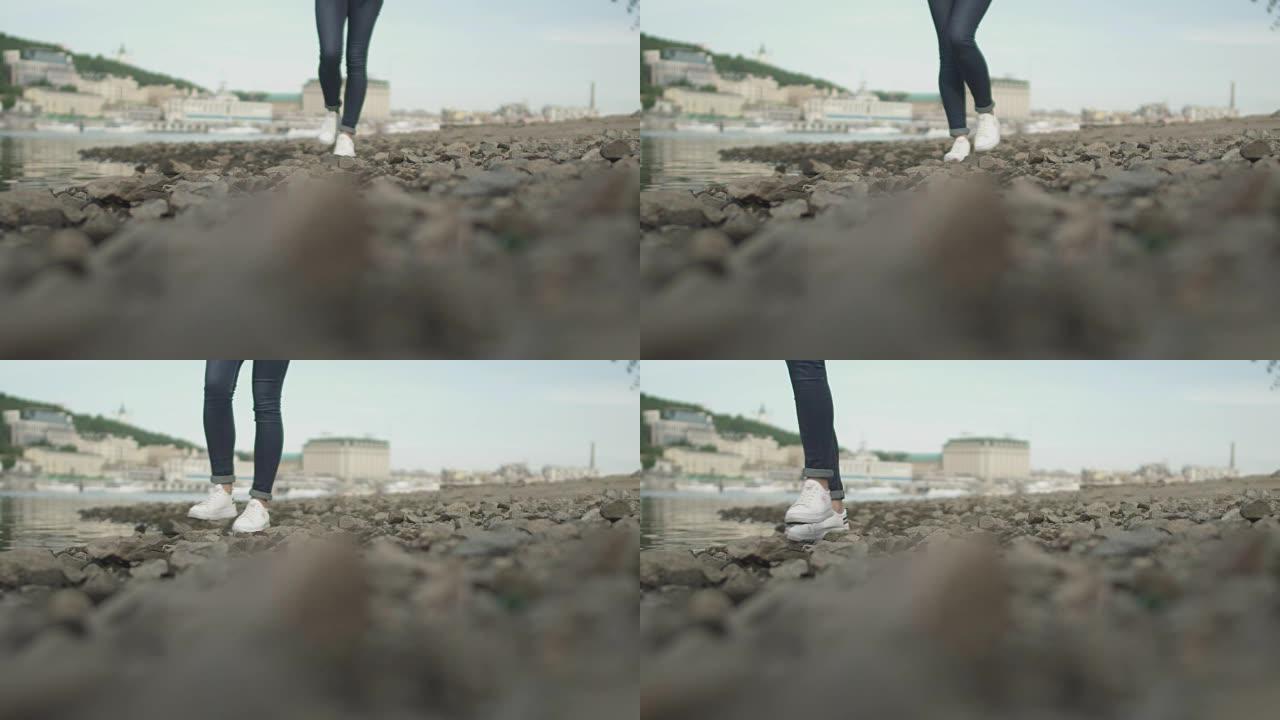 苗条女士的脚在河边的岩石上行走
