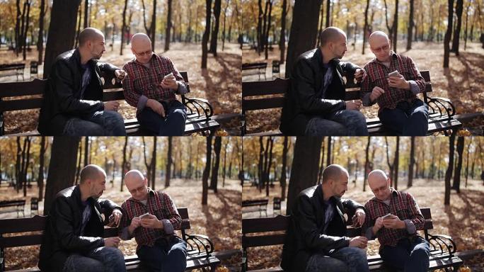 父亲和成年儿子一起坐在秋天公园的长凳上聊天。儿子在秋天的公园里和一位年迈的父亲打交道，他喝咖啡，教我