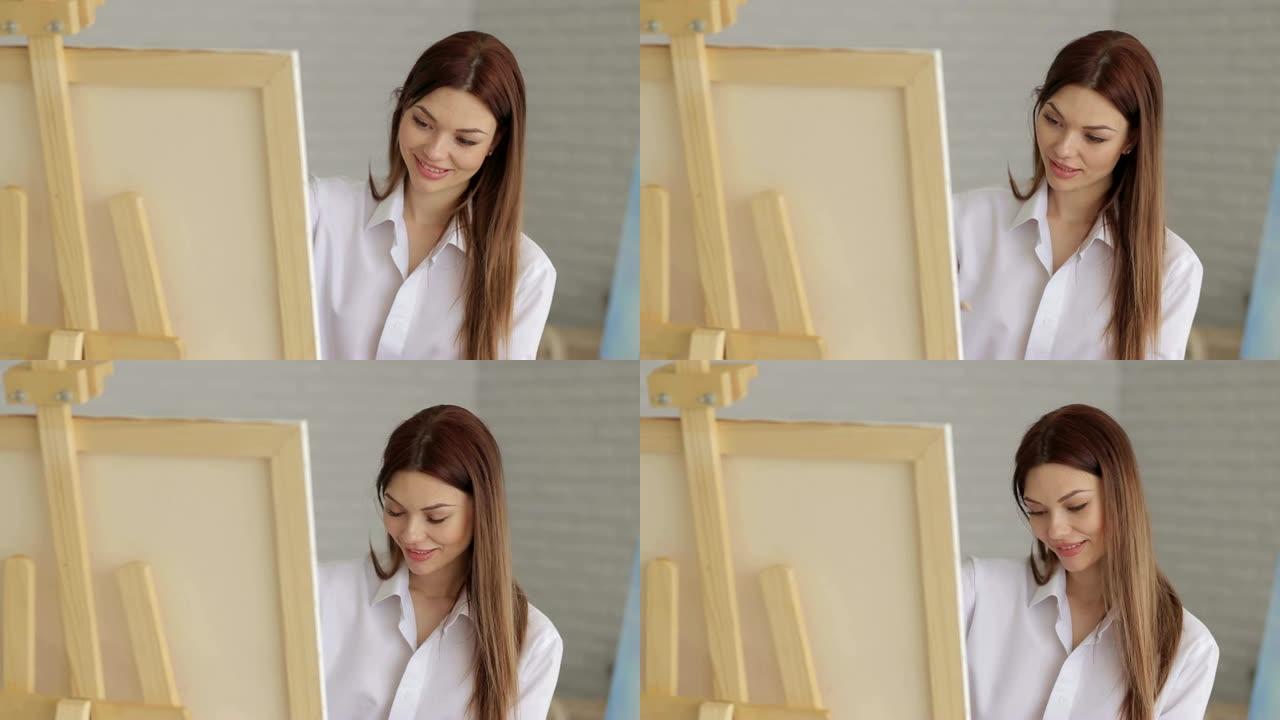 一个穿着白衬衫的年轻性感女孩在工作室的画布上画画。艺术