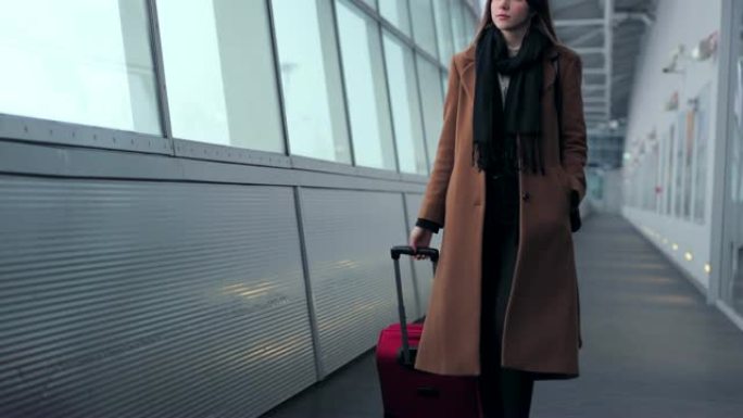 机场上的女商人在带手提行李在火车站或机场前往登机口时，在智能手机上聊天。女孩用手机交谈。