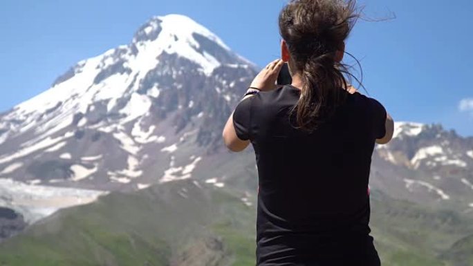 一名年轻女子正在用智能手机在山上拍下美丽的风景。