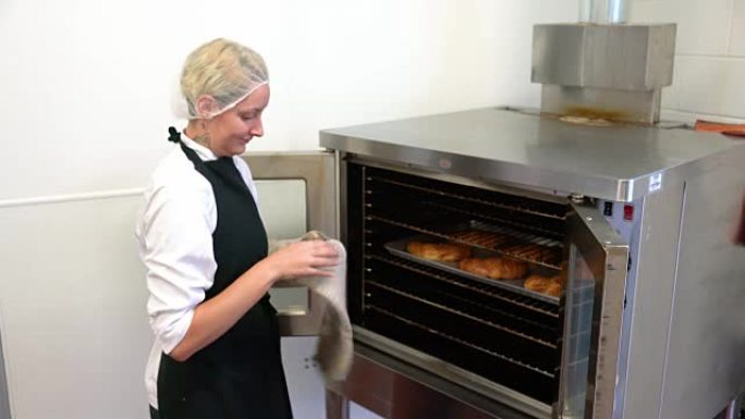 一位年轻的女面包师正确地使用烤箱手套携带热烤盘。