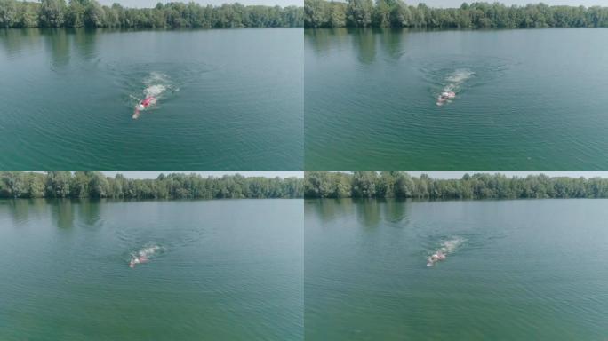 慢动作: 铁人铁人三项运动员男子训练的空中镜头。男子在铁人三项比赛的湖泊训练中游泳的无人机射击