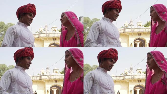 印度拉贾斯坦邦普什卡的一座寺庙外，穿着粉红色纱丽的美丽女子和戴着红色头巾的迷人男子