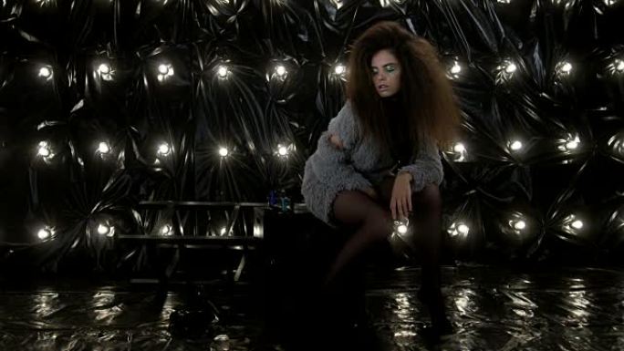 迷人的模特，非洲发型坐在黑色立方体上。时尚视频。