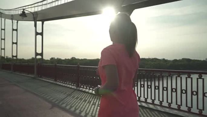 穿着紧身裤和t恤的可爱女孩正在桥上奔跑。慢动作