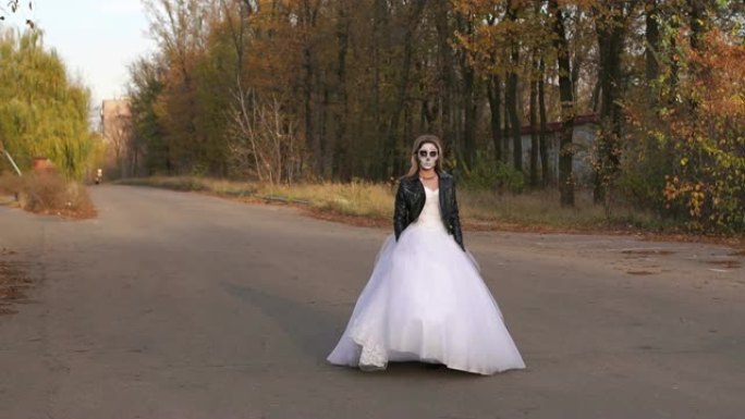 一个穿着婚纱的女孩在空荡荡的路上戴着骷髅面具。万圣节。