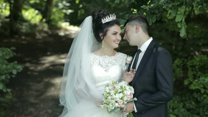 年轻美丽的新婚夫妇在公园里站在一起。可爱的新郎和新娘，带着婚礼花束。婚礼当天。慢动作