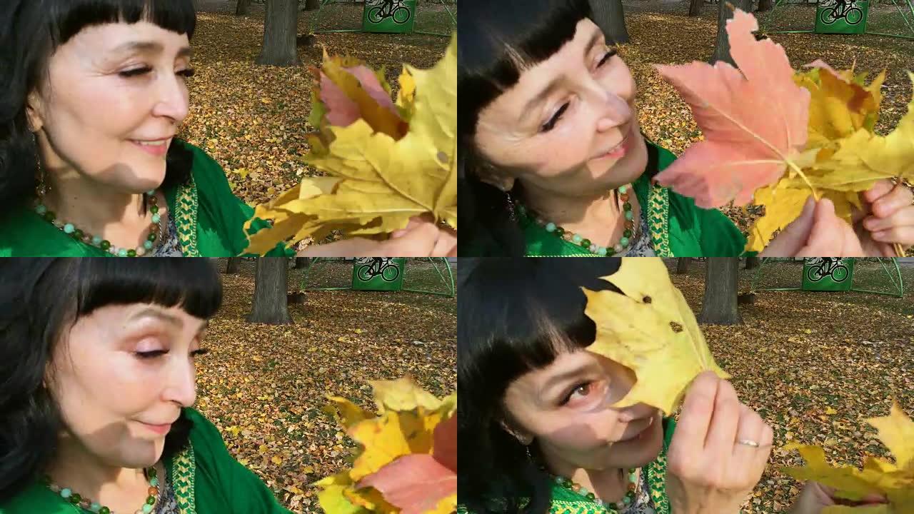 美丽的幸福女人穿着绿色的衣服在秋天的公园里整理和玩黄色的叶子。金秋概念。