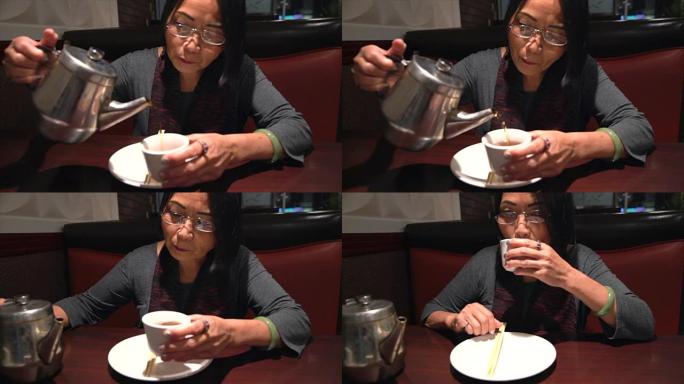 亚洲老妇人在餐馆里倒着热茶喝