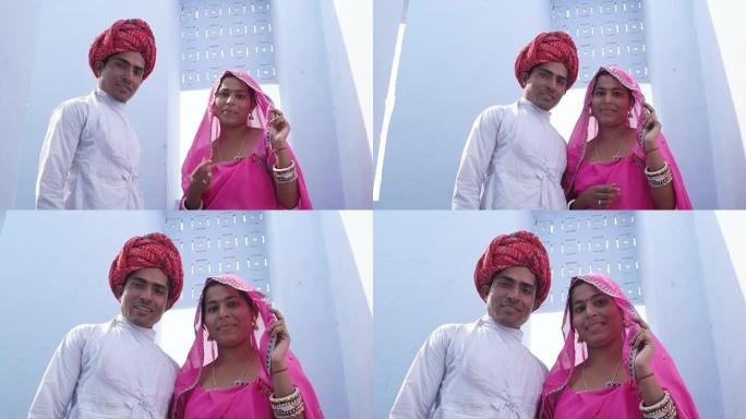 印度拉贾斯坦邦，一名女子身穿粉色纱丽，一名男子头戴红色头巾，背景为淡蓝色