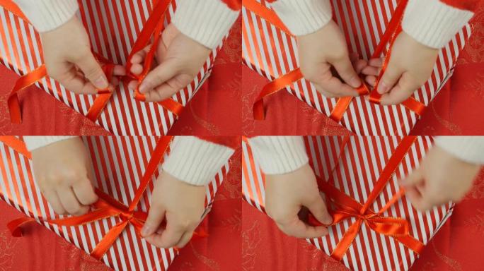 双手系在圣诞礼盒上的红色蝴蝶结