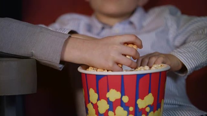 孩子们用手从纸盒里拿出爆米花。儿童电影食品