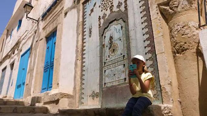 年轻女孩使用电话，坐在老城区传统阿拉伯门附近的台阶上
