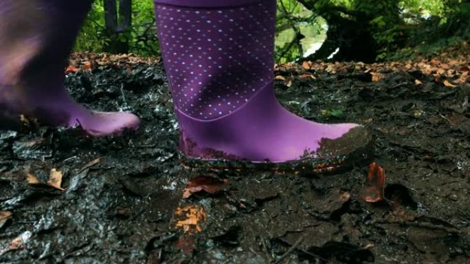年轻女孩带着雨靴穿过泥泞的水坑
