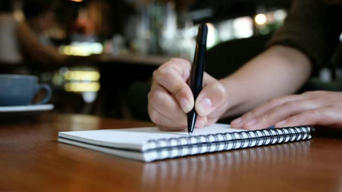 一个女人的手在咖啡馆的木桌上的空白笔记本上写字