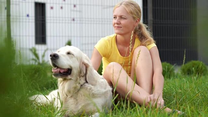 对宠物的爱 -- 一个年轻的金发女人和她的狗在草地上休息