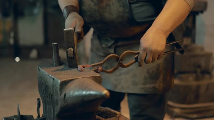 铁匠用钳子拿着马蹄铁，用锤子敲它。铁匠工作场所