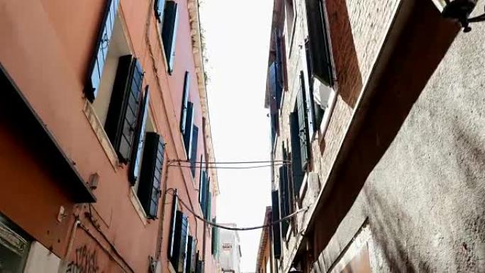 摄像机的跨度穿过威尼斯狭窄的街道，在旧的两层楼房屋之间，俯瞰天空