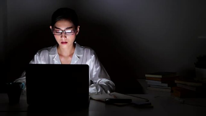 美丽的亚洲女人在电脑上工作，全神贯注，戴着眼镜。