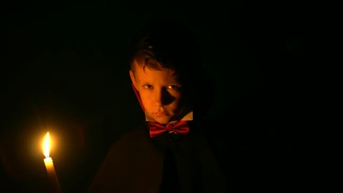 穿着吸血鬼服装的男孩在相机上摆姿势，在万圣节化妆成恶魔