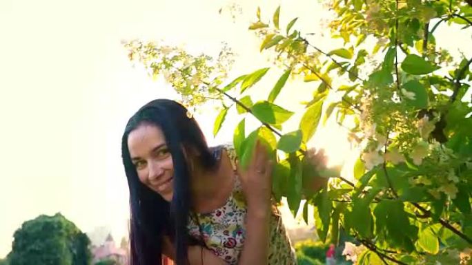 年轻女子在花园里嬉戏地绕着一棵绿树奔跑。一个微笑的黑发女人的肖像，脸颊凹陷，靠在绿色公园上。