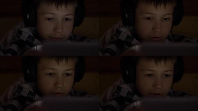 男孩在平板电脑上使用，躺在家里戴着耳机，在视频通信上进行对话，玩游戏