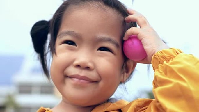 亚洲儿童/女孩特写脸微笑着拿着粉色球/玩具