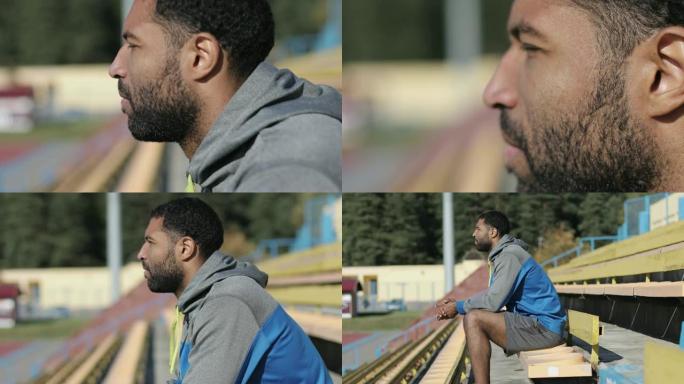 秋天，一个留着胡子穿着运动服的黑人坐在体育场上。