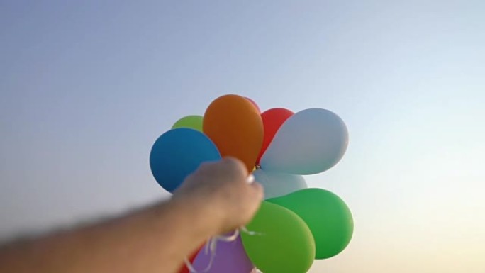 夏天，手拿着一堆彩色气球对着蓝天