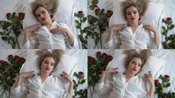 穿着短透明睡衣躺在床上的年轻漂亮女士的肖像。红玫瑰在靠近女性身体的床上。慢动作。