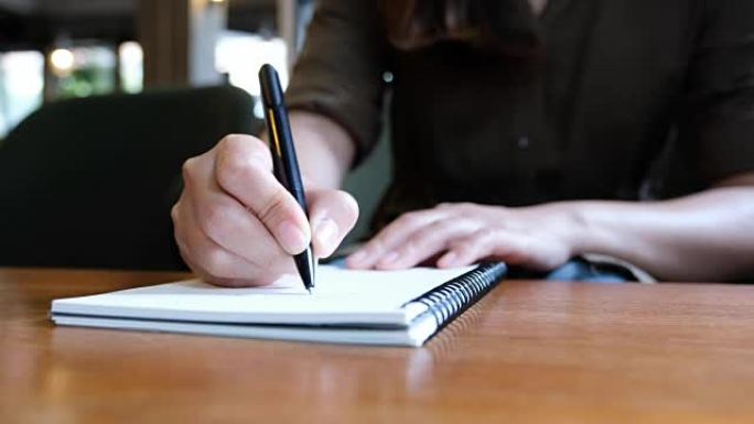 一个女人的手在木桌上的空白笔记本上写字