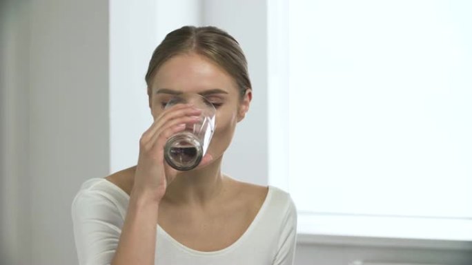 女人服用药丸，从白色内部的玻璃杯中喝水