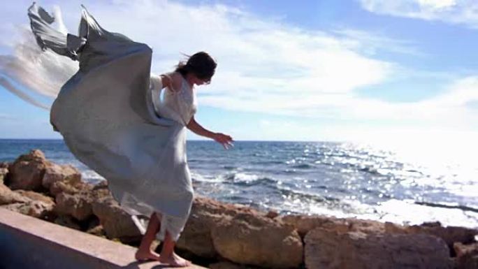 优雅的女人在岩石海岸跳跃。性感的女孩享受海景