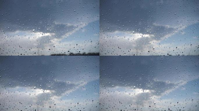 从雨滴到多云的天空的汽车挡风玻璃的角度。雨天关闭车辆窗玻璃上的水滴。
