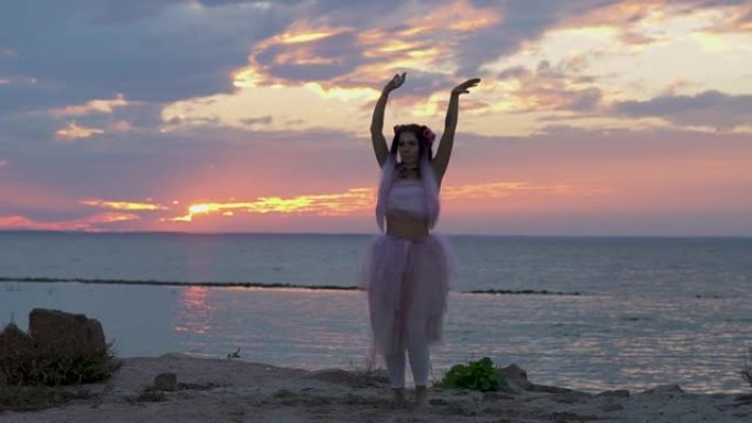 可爱的女人，穿着粉红色的连衣裙在河岸上跳舞，妆容鲜艳。一个性感女孩的舞蹈，有着美妙的发型和鲜花。慢动
