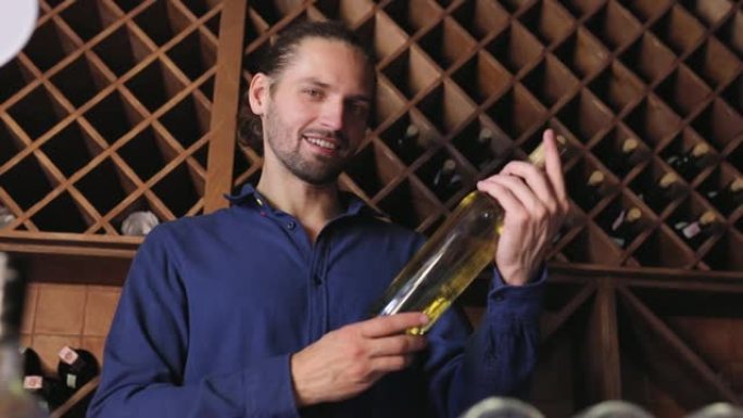 微笑的男人在酒庄餐厅的酒窖里喝一瓶葡萄酒