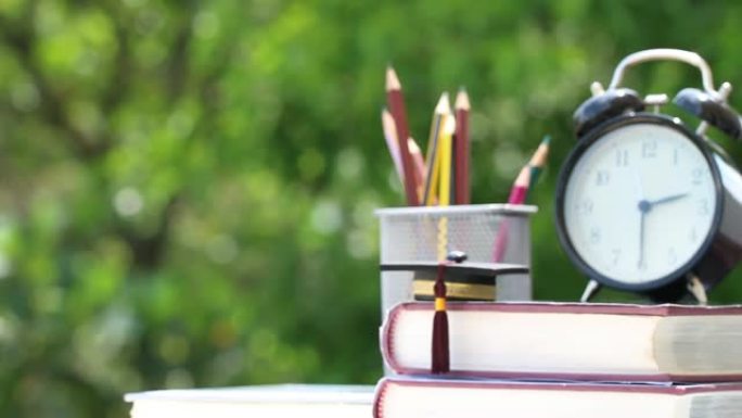 研究生或教育知识出国学习概念: 教科书上的毕业帽，笔盒和桌子上的复古时钟，模糊绿色背景。回到学校