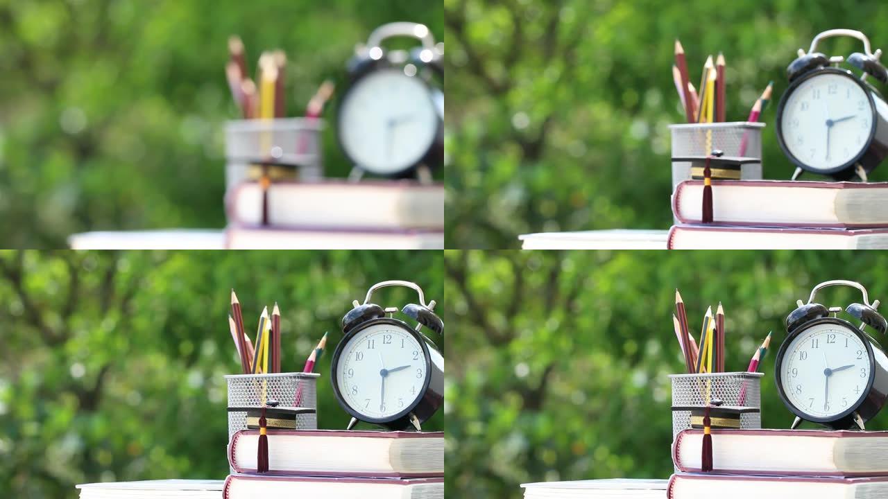 研究生或教育知识出国学习概念: 教科书上的毕业帽，笔盒和桌子上的复古时钟，模糊绿色背景。回到学校