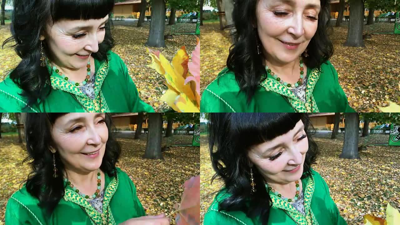 美丽的幸福女人穿着绿色的衣服在秋天的公园里整理和玩黄色的叶子。金秋概念。