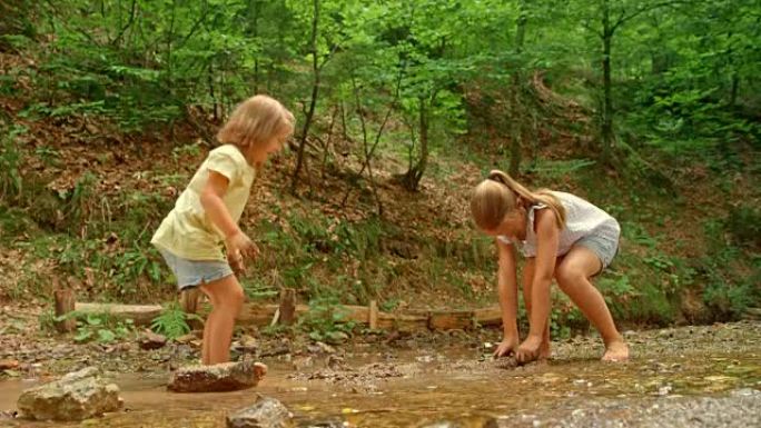 SLO MO两个姐妹站在一条小森林小溪中互相扔泥