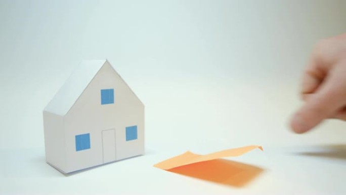 手放在纸质房屋购买房屋的标志旁边，橙色张贴
