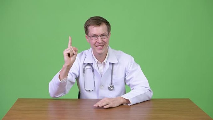 快乐的男人医生坐着微笑着指着手指