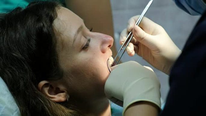 口腔科医生将棉签放在女人的嘴里，助手用牙齿上的聚合紫外线灯照射到病人的牙齿上。去看牙医