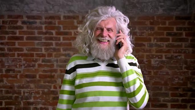 有趣的白发和浓密胡须的白人老人，挂在手机上，与笑脸，幸福插图，红砖背景交谈