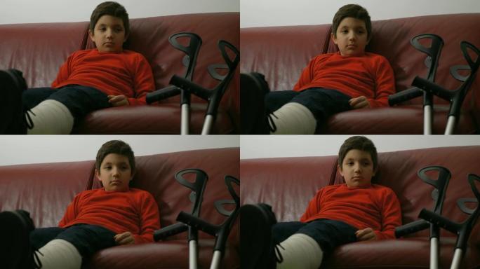 悲伤受伤的孩子坐在沙发上看着拐杖