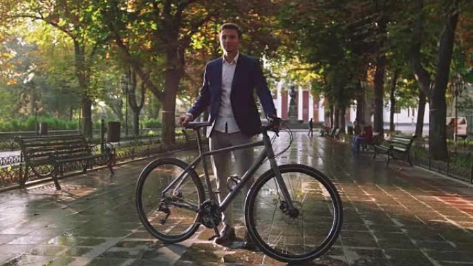 日出时，英俊的年轻人骑着自行车站在市中心的公园里，慢动作的肖像