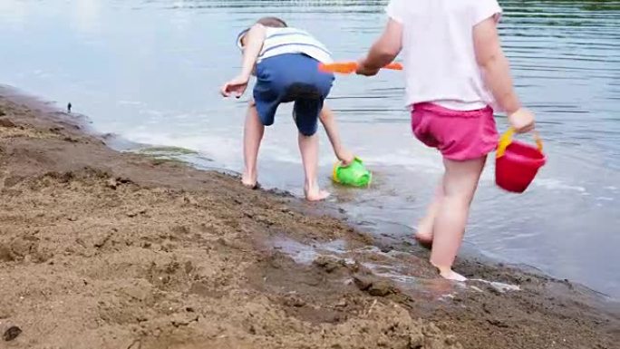 小女孩和男孩用水桶从河里打水，动作缓慢。孩子们在沙滩上的沙滩上玩耍